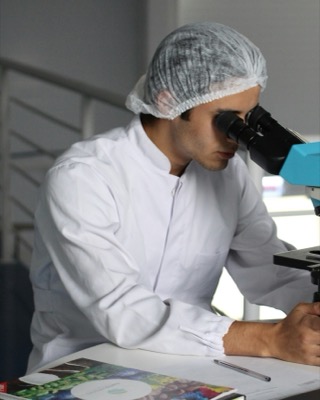 Researcher in a lab coat and hairnet looking through a microscope